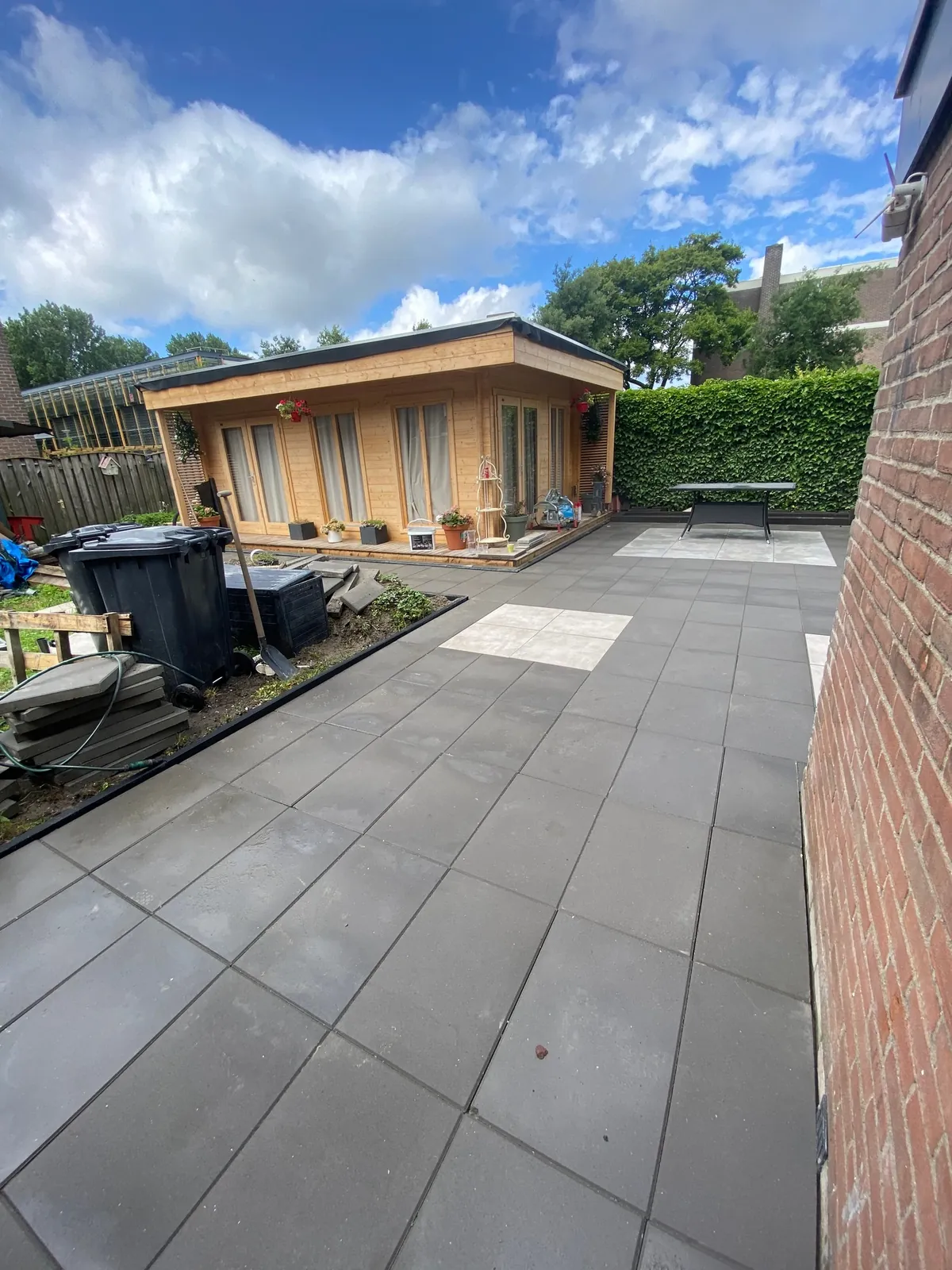 Antraciet terras met lichte accenttegels voor een houten tuinhuis