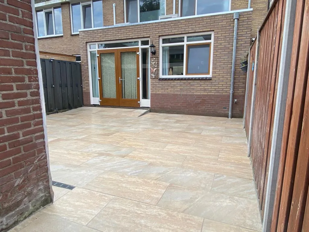 Terras van grote tegels in zandtinten achter een woning